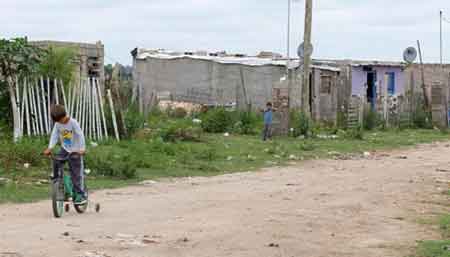 Nio en bicicleta, otro lo observa. En el fondo se ve la villa miseria